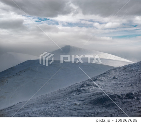 Snow covered mountain slope in last evening sunlight. Magnificent windy dusk on tops above picturesque alpine ski resort, Dragobrat, Ukraine, Carpathian Mountains. Snow covered mountain slope in last evening sunlight. Magnificent windy dusk on tops above picturesque alpine ski resort, Dragobrat, Ukraine, Carpathian Mountains. 109867688
