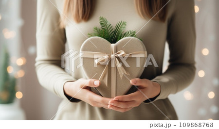 a woman holds a heart shaped gift box with a green ribbon 109868768