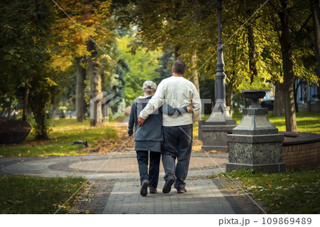 An elderly couple, man and woman walk in the autumn park. 109869489