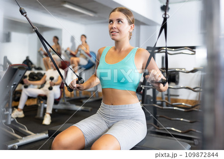Active athlete young woman during exercises on crossover exercise machine with loops and weighting Active athlete young woman during exercises on crossover exercise machine with loops and weighting 109872844
