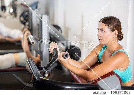 Young woman trains her arm muscles on machine Young woman trains her arm muscles on machine 109873068