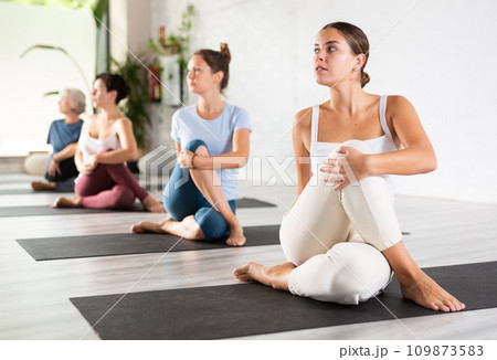 Calm female gym visitor twisting in Ardha Matsyendrasana pose during group yoga training 109873583