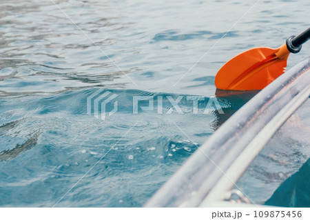 Woman in kayak back view. Happy young woman with long hair floating in transparent kayak on the crystal clear sea. Summer holiday vacation and cheerful female people relaxing having fun on the boat Woman in kayak back view. Happy young woman with long hair floating in transparent kayak on the crystal clear sea. Summer holiday vacation and cheerful female people relaxing having fun on the boat 109875456