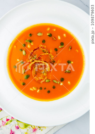 orange cream soup with pieces of meat in a white plate, top view 109879603