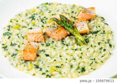 rice porridge with artichoke, red fish and herbs in a white plate, side view 109879613