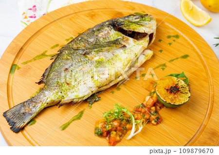 baked fish with lime and spices on a wooden tray on a marble background, side view 109879670
