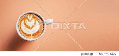 Minimalist coffee cup on peach fuzz colored table. Cup of coffee in Peach Fuzz color. top view, banner. color of year 2024. Peach Fuzz cup of cappuccino coffee 109882863