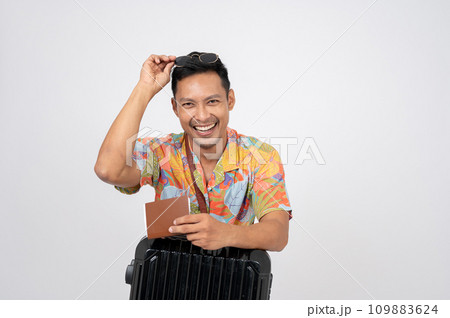 A happy Asian man in summer clothes is posing with his passport and luggage, isolated background. 109883624