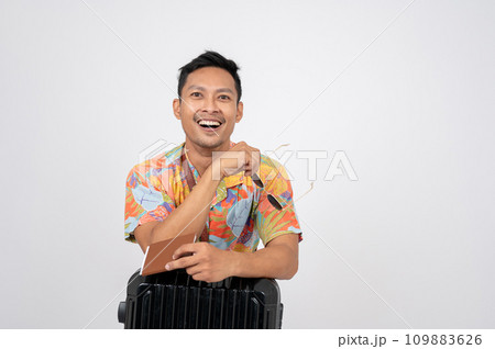 A happy Asian man in summer clothes is posing with his passport and luggage, isolated background. 109883626