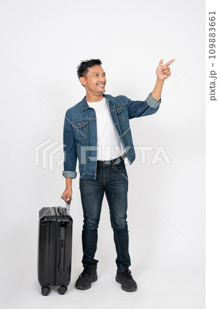 A positive Asian man with his luggage is pointing his finger at an empty space, isolated background. 109883661