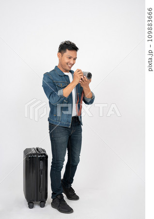 A positive Asian man tourist is taking pictures with his camera, standing on an isolated background 109883666