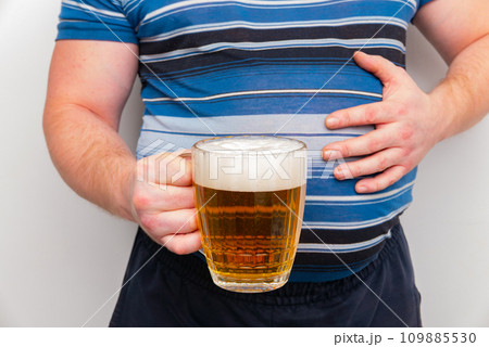 A pot-bellied man holds a mug of beer in his hand. Isolated on a white background. 109885530