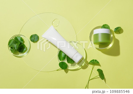 An unlabeled cosmetics set, fresh pennywort and transparent glass platforms are displayed on the background. Scene for vegan cosmetics advertisement. 109885546