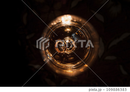 Gold wedding rings on a brown background. Gold wedding rings in a glass of champagne Gold wedding rings on a brown background. Gold wedding rings in a glass of champagne 109886383