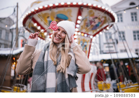 Portrait of young smiling woman holding heart shape lollipop in winter time outdoors. Portrait of young smiling woman holding heart shape lollipop in winter time outdoors. 109888503