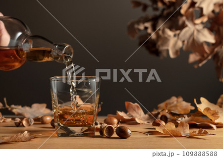 Whiskey on a wooden table with dried-up oak leaves. Whiskey on a wooden table with dried-up oak leaves. 109888588