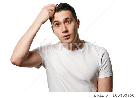 Portrait of attractive young man looks at camera in surprise while combing his hair against white background. Concept of hair care, barber. Portrait of attractive young man looks at camera in surprise while combing his hair against white background. Concept of hair care, barber. 109890350