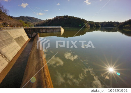 打上調整池の洪水吐と湖面に反射する太陽 109891991