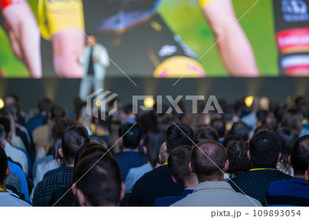 Back view of businesspeople listening to male speaker on stage during global presentation at conference hall Back view of businesspeople listening to male speaker on stage during global presentation at conference hall 109893054