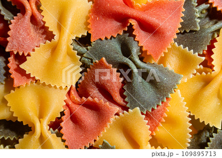 Dry Uncooked Colored Farfalle Pasta and Raw Macaroni on a Textured Background Dry Uncooked Colored Farfalle Pasta and Raw Macaroni on a Textured Background 109895713