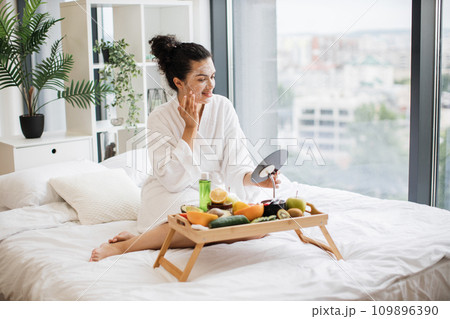 Relaxed adult person in after-shower wear applying facial mask Relaxed adult person in after-shower wear applying facial mask 109896390
