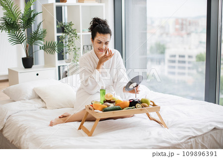 Relaxed adult person in after-shower wear applying facial mask 109896391