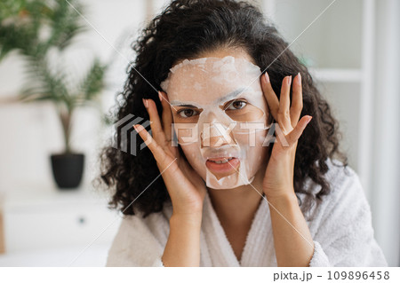 Woman in after-shower outfit touching cosmetic mask fixed on face 109896458