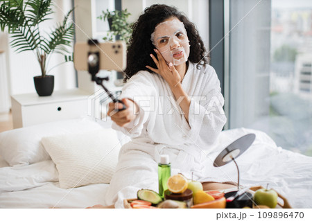 Young female influencer in paper sheet mask holding smartphone 109896470
