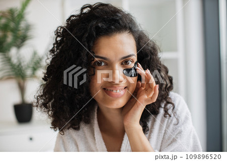African-american woman in white bathrobe fixing black gel patch with finger 109896520