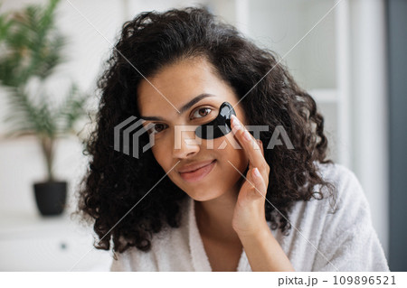 African-american woman in white bathrobe fixing black gel patch with finger 109896521