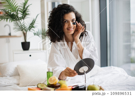 Woman in after-shower outfit putting anti-aging gel patch under eye Woman in after-shower outfit putting anti-aging gel patch under eye 109896531