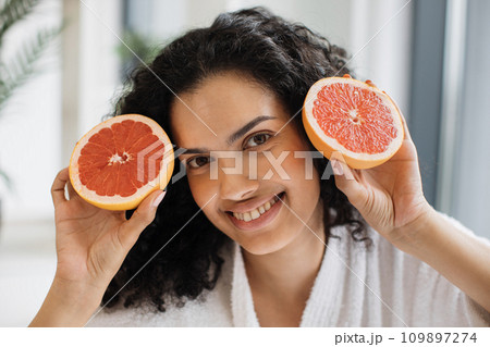 Healthy female holding two halves of grapefruit near cheeks Healthy female holding two halves of grapefruit near cheeks 109897274