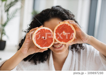 Female in white bathrobe covering eyes with grapefruit halves 109897280