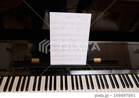 Still life of old vintage black piano with ebony and ivory keys and white paper sheet with musical notes of classic melody or composition. Classic luxury chord instrument 109897801
