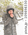 a boy is posing with snow on the street, it is snowing, a blizzard and frost on a winter day, he warms his hands with his breath 109898330