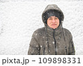 a boy is posing on snow background outdoor, it is snowing, a blizzard and frost on a winter day 109898331