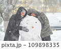a girl and a boy is playing with snow on the street, making snowman, it is snowing, a blizzard and frost on a winter day 109898335