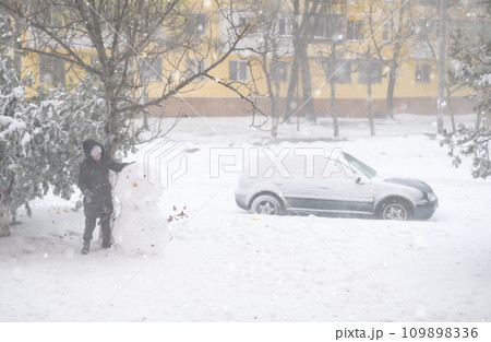 a girl is playing with snow on the street, making snowman, it is snowing, a blizzard and frost on a winter day 109898336