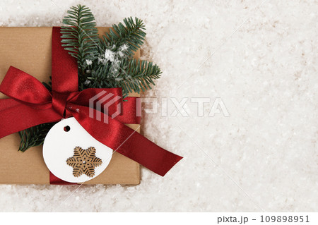Card with gift box with fir tree sprig and label with snowflake on snow background. Space for your text. 109898951