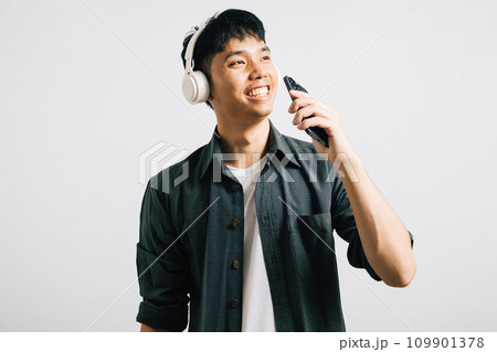 A man is excited and smiling, singing along to music on his smartphone using Bluetooth earphones. Studio shot isolated on white background, highlighting his passion for karaoke. A man is excited and smiling, singing along to music on his smartphone using Bluetooth earphones. Studio shot isolated on white background, highlighting his passion for karaoke. 109901378