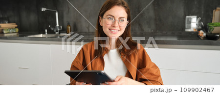 Portrait of beautiful young brunette woman, holding digital tablet, reading with glasses, smiling, surfing the net using gadget 109902467