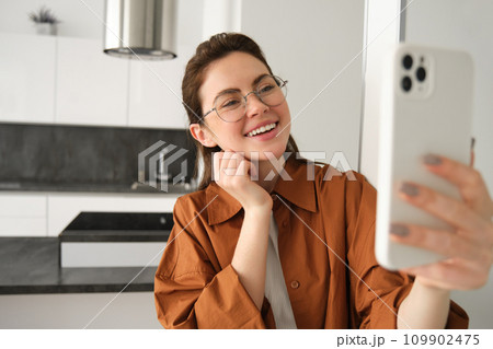 Happy smiling woman in glasses, taking selfie, recording video on smartphone, video chats on mobile phone application Happy smiling woman in glasses, taking selfie, recording video on smartphone, video chats on mobile phone application 109902475