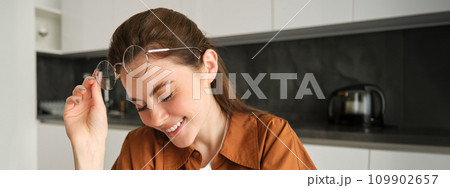 Portrait of young happy woman, sitting in kitchen, wearing glasses, reading or working from home Portrait of young happy woman, sitting in kitchen, wearing glasses, reading or working from home 109902657
