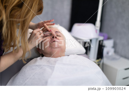 A woman lies on a bed in a beauty salon and speaks to her beautician. A woman lies on a bed in a beauty salon and speaks to her beautician. 109903024