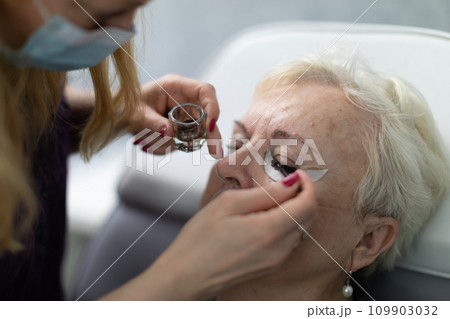 A beauty salon employee works with a client, painting her eyelashes. A beauty salon employee works with a client, painting her eyelashes. 109903032