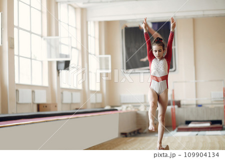 Child gymnastics balance beam. Girl gymnast athlete during an exercise horizontal bar in gymnastics competitions. Child gymnastics balance beam. Girl gymnast athlete during an exercise horizontal bar in gymnastics competitions. 109904134