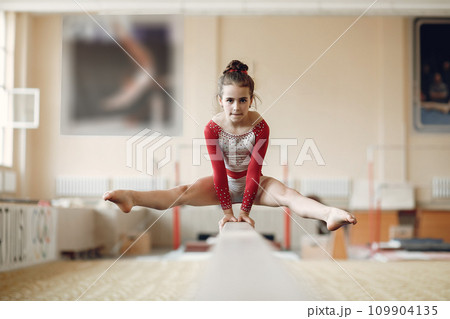 Child gymnastics balance beam. Girl gymnast athlete during an exercise horizontal bar in gymnastics competitions. Child gymnastics balance beam. Girl gymnast athlete during an exercise horizontal bar in gymnastics competitions. 109904135
