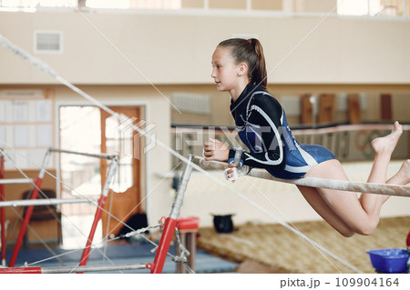 Child gymnastics balance beam. Girl gymnast athlete during an exercise horizontal bar in gymnastics competitions. Child gymnastics balance beam. Girl gymnast athlete during an exercise horizontal bar in gymnastics competitions. 109904164