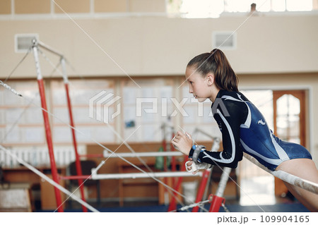 Child gymnastics balance beam. Girl gymnast athlete during an exercise horizontal bar in gymnastics competitions. Child gymnastics balance beam. Girl gymnast athlete during an exercise horizontal bar in gymnastics competitions. 109904165