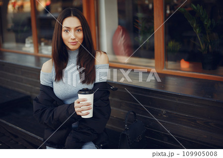 Beautiful girl in a city. Stylish girl drinking a coffee. Lady in a gray dress 109905008